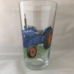 May include: A blue and orange tractor design on a clear glass pint glass.