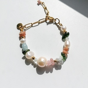 Può includere: Un braccialetto a catena dorata con chiusura a moschettone, con una varietà di pietre e perle color pastello. Le pietre includono rosa, verde e bianco.