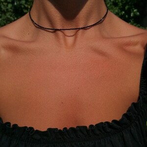 Puede incluir: Un delicado collar negro de choker hecho de peque&ntilde;as cuentas redondas. El collar lo lleva una persona con la piel bronceada.