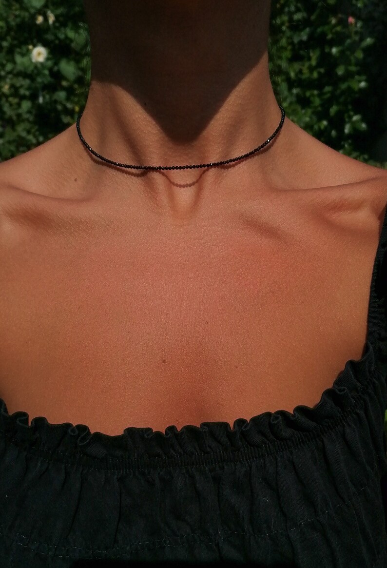 Puede incluir: Un delicado collar negro de choker hecho de peque&ntilde;as cuentas redondas. El collar lo lleva una persona con la piel bronceada.