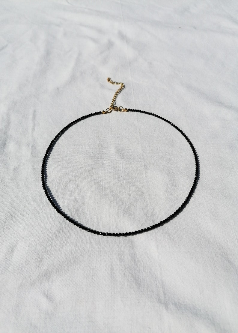 Puede incluir: Un delicado collar negro de choker hecho de peque&ntilde;as cuentas con un cierre dorado.