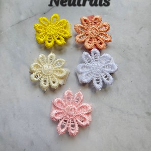 May include: Five small flower-shaped hair clips in various neutral colors: yellow, orange, white, light pink, and pink. The clips are made of lace and have a simple design.