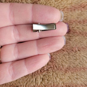 May include: A silver metal hair clip with a smooth, rectangular surface.