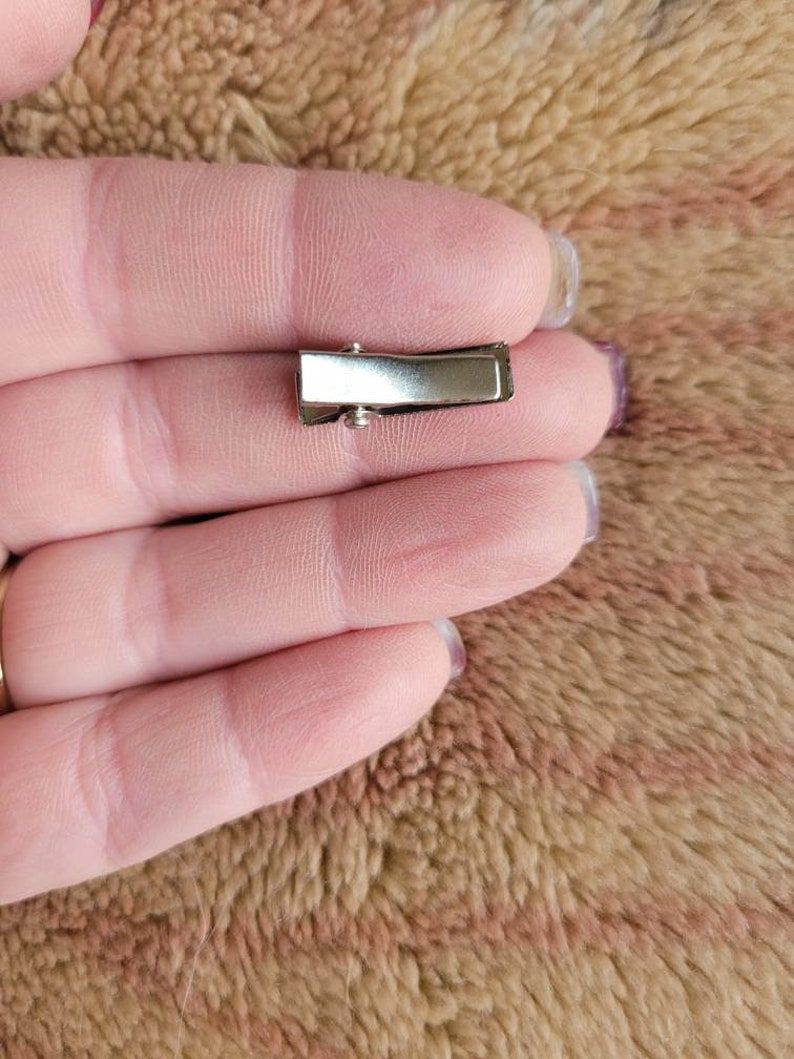 May include: A silver metal hair clip with a smooth, rectangular surface.