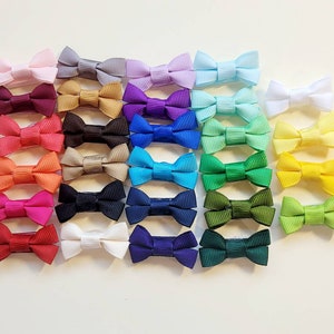 May include: A collection of 25 mini hair bows in various colors, including pink, red, orange, yellow, green, blue, purple, and black. The bows are made of ribbon and are attached to alligator clips.