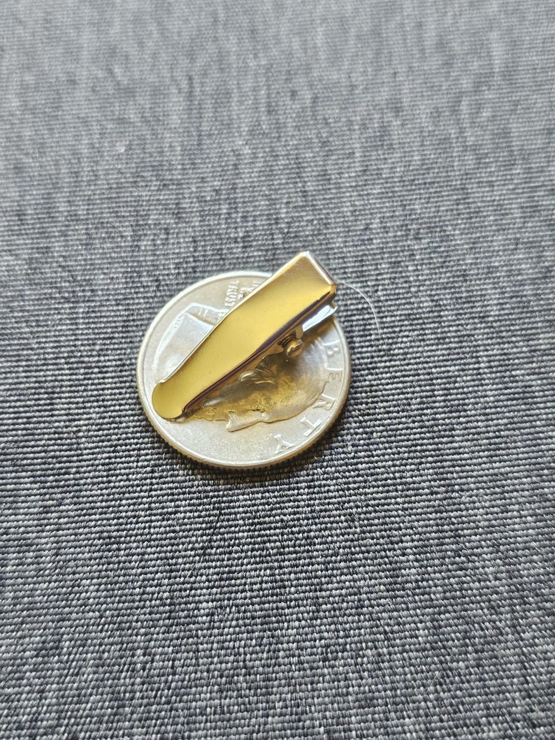 May include: A gold metal alligator clip, approximately the size of a US quarter, for hair or crafts.