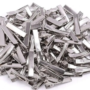 May include: A large pile of silver metal hair clips. The clips are all the same size and shape, and they are arranged in a random pattern.