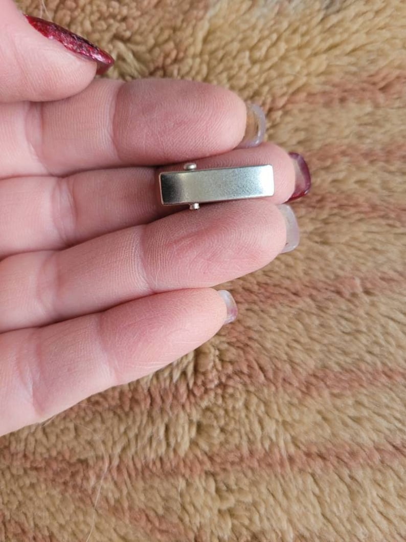 May include: A silver-toned metal clasp for a bracelet or necklace. The clasp is rectangular in shape and has a smooth, polished finish.