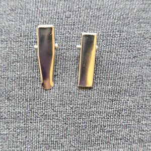 May include: Two silver metal hair clips, one slightly larger than the other, on a gray textured background.