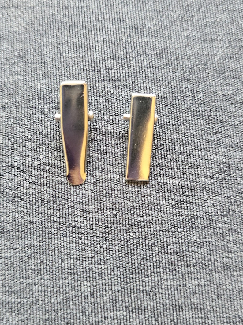 May include: Two silver metal hair clips, one slightly larger than the other, on a gray textured background.
