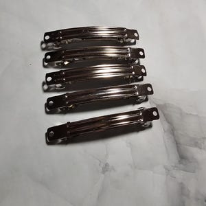 May include: Six silver metal hair clips. The clips are all the same size and shape, and they are arranged in a row.