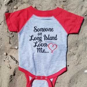 May include: A gray and red baby onesie with the text "Someone on Long Island Loves Me..." and a red heart.