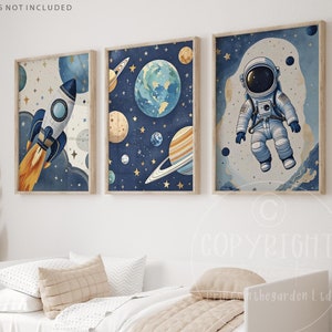 May include: Three space-themed prints featuring a rocket, planets, and an astronaut. The prints are in a blue and white colour scheme with gold accents. The prints are framed and ready to hang.