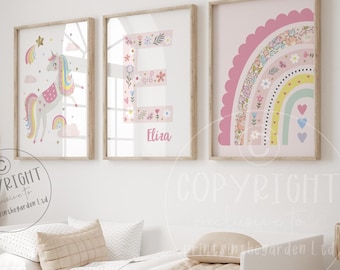 May include: Three framed prints with a pink background. The first print features a unicorn with a rainbow and stars. The second print features the letter E with floral designs and the name Elira. The third print features a rainbow with floral designs and hearts.