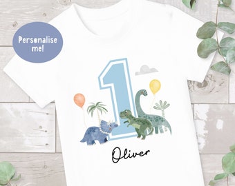 May include: White t-shirt with a blue number one, two dinosaurs, and the name Oliver printed on it. The shirt is personalized with the name Oliver.