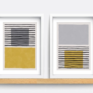 May include: Two framed abstract art prints featuring black and white stripes and geometric shapes in yellow and grey.