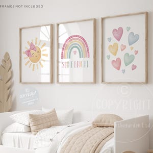 May include: Three watercolour prints for a nursery or child's room. The prints feature a sun with a smiling face and a pink bow, a rainbow with the text "Shine Bright", and a cluster of pastel hearts.