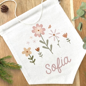May include: A white canvas banner featuring a floral design in pink, orange, and green. The banner is personalised with the name "Sofia" written in pink cursive lettering.