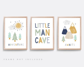 May include: Three framed prints with a woodland theme. The first print features a yellow sun, green trees, and the text "Adventure". The second print features the text "Little Man Cave" in blue, yellow, and green. The third print features blue and yellow mountains, green trees, and the text "Awaits".
