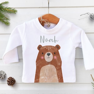 May include: White long-sleeved baby shirt with a brown bear illustration and the name "Noah" printed in grey.