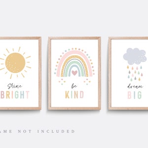 May include: Three printable wall art prints featuring a sun, rainbow, and cloud with raindrops. The sun is yellow with a white outline and has the text "Shine Bright". The rainbow is pink, yellow, green, and blue with a white outline and has the text "Be Kind". The cloud is grey with a white outline and has the text "Dream Big".