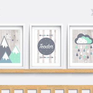 May include: Three framed prints with a woodgrain background. The first print features a mountain range with blue and green accents. The second print has a grey circle with the name "Teodor" in white text. The third print has a grey and green cloud with raindrops.