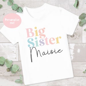 May include: White t-shirt with the text "Big Sister" in colorful letters and the name "Maisie" written in cursive below.