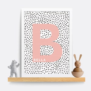 Puede incluir: Una impresi&oacute;n enmarcada con una letra "B" rosa sobre un fondo blanco con lunares negros. El nombre "BELLA" est&aacute; impreso debajo de la letra.