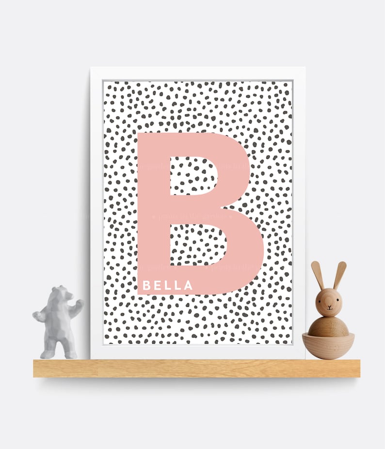 Puede incluir: Una impresi&oacute;n enmarcada con una letra "B" rosa sobre un fondo blanco con lunares negros. El nombre "BELLA" est&aacute; impreso debajo de la letra.
