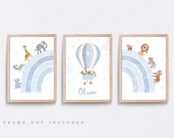 May include: Three watercolor prints featuring a blue rainbow with various animals. The first print shows a zebra, elephant, giraffe, and rhino walking on the rainbow. The second print shows a hot air balloon with a star and the name "Oliver" written below. The third print shows a lion, monkey, hippopotamus, and tiger walking on the rainbow.