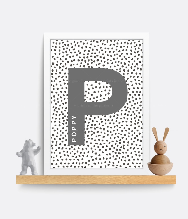 Puede incluir: Una impresi&oacute;n enmarcada en blanco con un fondo de lunares blanco y negro. La letra "P" es gris y el nombre "Poppy" est&aacute; escrito verticalmente en gris dentro de la letra. El texto "prints in the garden" est&aacute; escrito en gris en la parte superior e inferior de la letra.