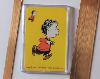 Op de afbeelding: Een gele kaart met een zwart-wit cartoon afbeelding van een jongen die rent. De tekst op de kaart luidt "COPR. © 1950, 1952 UNITED FEATURE SYNDICATE, INC."