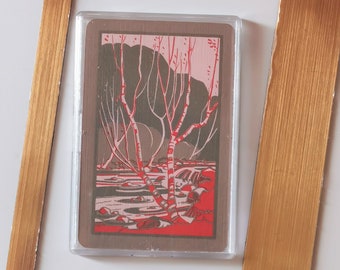 Op de afbeelding: Een vintage speelkaart met een rode en witte illustratie van bomen in een bos. De kaart is ingelijst in een gouden lijst.