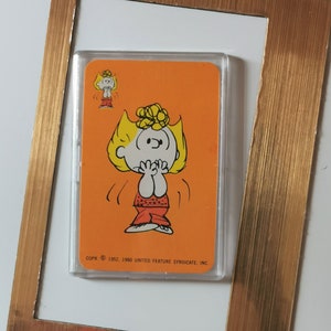 May include: A vintage Peanuts character card featuring a cartoon of Peppermint Patty with blonde hair and a red and white outfit. The card is orange and has the text "COPR. © 1952, 1960 UNITED FEATURE SYNDICATE, INC."