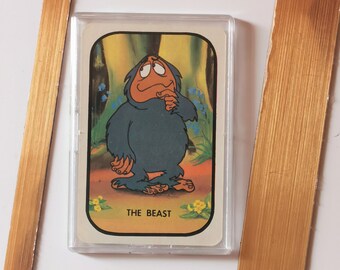 Op de afbeelding: Een vintage verzamelkaart met een cartoonillustratie van een blauw beest met een bruin gezicht op een gele achtergrond. De kaart heeft de tekst "THE BEAST" onderaan gedrukt.