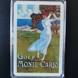 May include: A vintage postcard featuring a woman in a white dress playing golf on a green course with a view of the ocean and a town in the distance. The text "GOLF MONTE-CARLO" is printed at the bottom of the postcard.