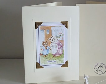 Op de afbeelding: Een crèmekleurige kaart met een gouden omlijsting rond een afbeelding van twee katten. De afbeelding heeft de titel "Tom Kitten". De kaart is blanco aan de binnenkant en heeft een crèmekleurige envelop. De kaart is van Fuzzy Mouse.