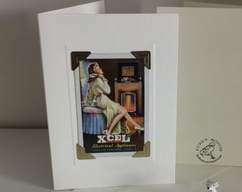 Op de afbeelding: Een vintage-groetkaart met een vrouw in een witte badjas die voor een open haard zit. De kaart heeft een gouden rand en de tekst "XCEL Electrical Appliances" staat onderaan gedrukt. De kaart is blanco aan de binnenkant en perfect om een speciale boodschap te sturen.