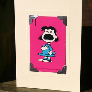May include: A vintage card with a pink background and a black and white illustration of a girl with her mouth open, as if she is yelling. The card has a silver frame with decorative corners and the text "&copy; 1950, 1952 UNITED FEATURE SYNDICATE".