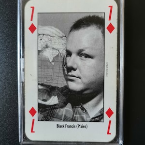 May include: A playing card featuring a black and white photo of Black Francis from the band Pixies. The card is a 7 of diamonds.