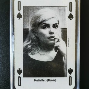 May include: A black and white playing card featuring a photo of Debbie Harry (Blondie) as the Queen of Spades. The card is in a plastic protective case.