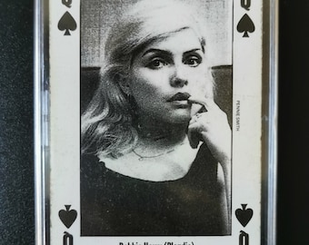 Op de afbeelding: Een zwart-witte speelkaart met een foto van Debbie Harry (Blondie) als Dame Schoppen. De kaart zit in een plastic beschermhoesje.