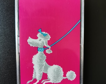 Op de afbeelding: Een rechthoekige, doorzichtige plastic hoes met een roze achtergrond met een illustratie van een witte poedel. De poedel heeft een blauwe strik, halsband en riem. De poedel zit en kijkt naar links.