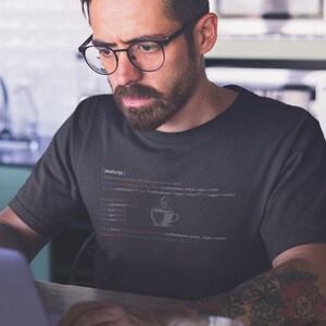 May include: A dark gray t-shirt with a white graphic of code that reads "(JavaScript)" and "function to calculate the flavor of regular coffee (coffeebeans, water, sugar, cream)". A small white coffee cup icon is in the code.