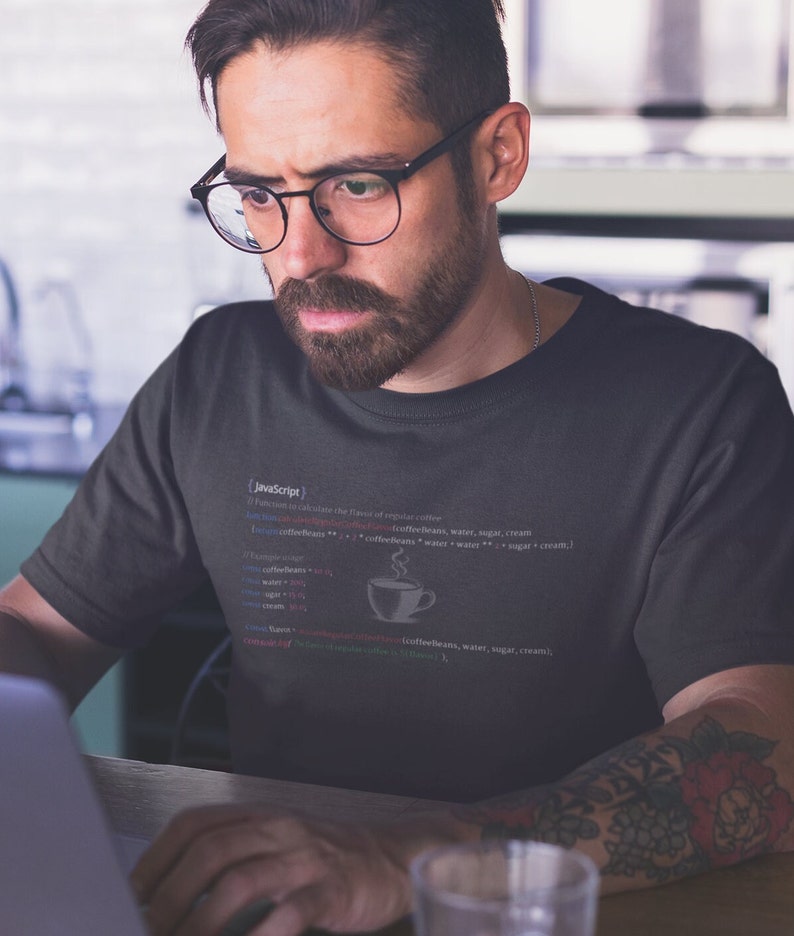 May include: A dark gray t-shirt with a white graphic of code that reads "(JavaScript)" and "function to calculate the flavor of regular coffee (coffeebeans, water, sugar, cream)". A small white coffee cup icon is in the code.