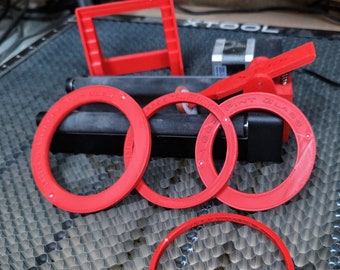 May include: Four red plastic rings, two with the text "PRINT GLASS" and two with the text "XTOOL", on a gray honeycomb surface.