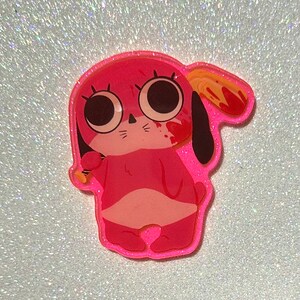 Puede incluir: Encanto de acrílico rosa con purpurina de un perro de dibujos animados con ojos grandes, sosteniendo un cuchillo ensangrentado. El perro lleva un atuendo rosa y tiene una oreja ensangrentada.