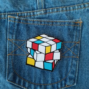 May include: A colorful Rubik's Cube patch sewn onto a blue denim pocket.