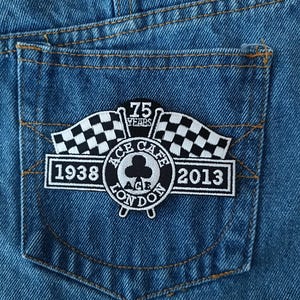 May include: A black and white embroidered patch on a blue denim background. The patch features a checkered flag, the words "Ace Cafe London", a clover, and the years "1938" and "2013". The text "75 Years" is also included.