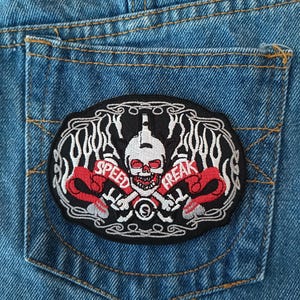 May include: Embroidered patch with a skull and the words "SPEED FREAK" on a denim pocket. The patch features a skull with a bottle and flames, with red and white accents.